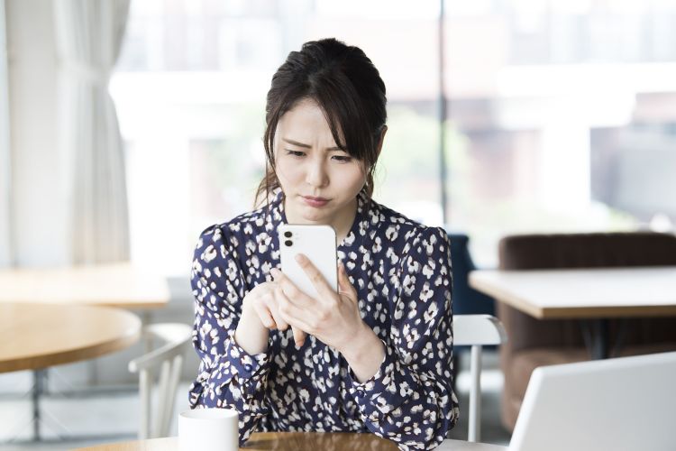 スマホの画面を見て悩む女性